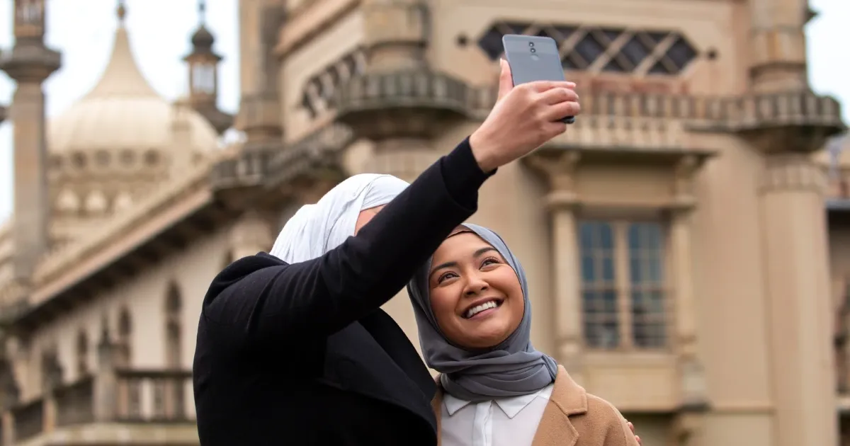 Two women in hijab taking a selfie with UAE Golden Visa at Dubai landmark